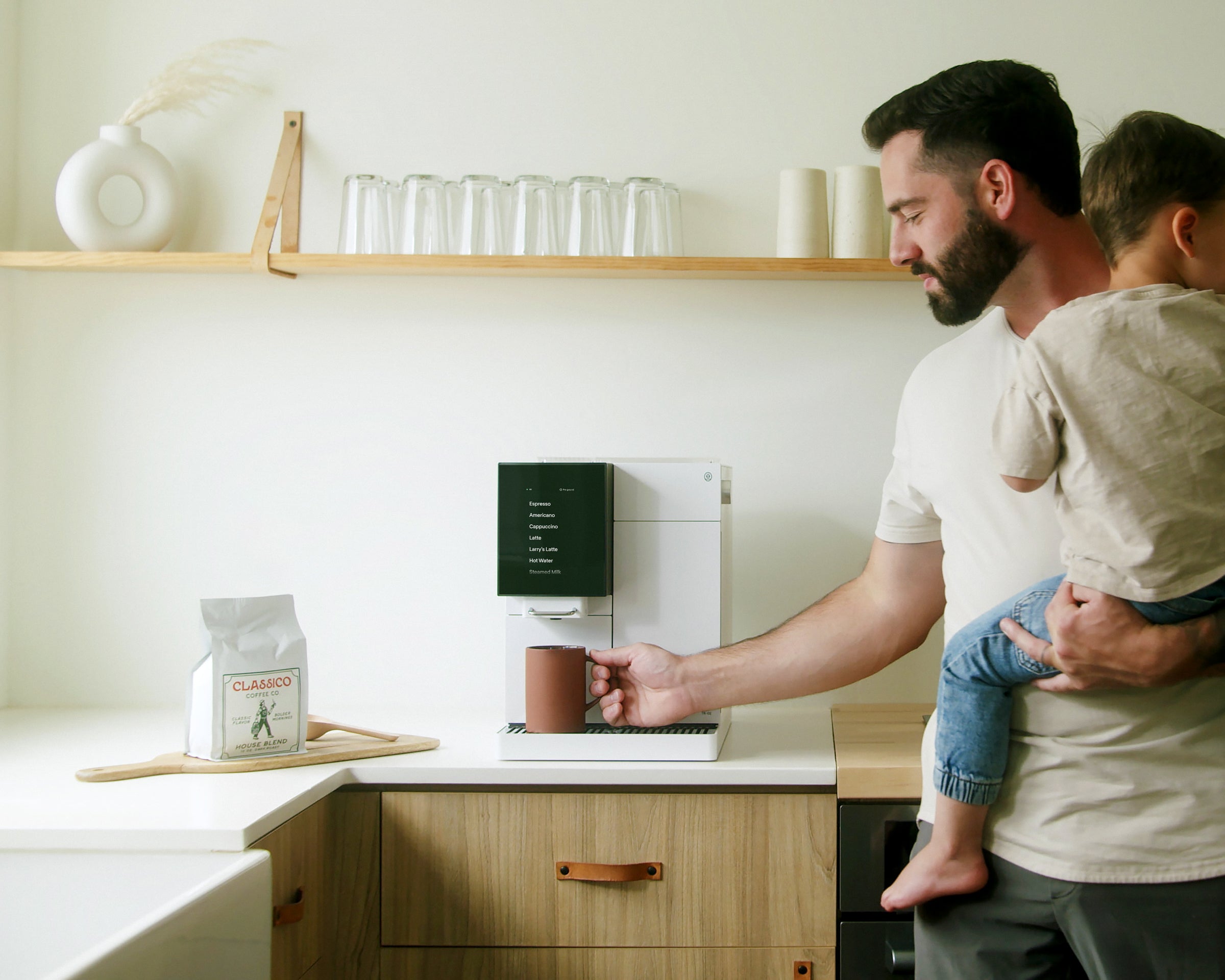 Brown Haired man with child grabbing a red mug off of a white TK-02 on a kitchen counter